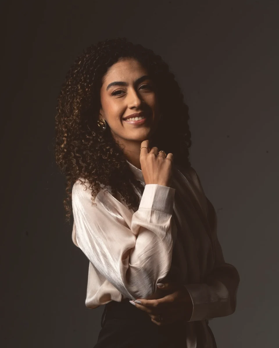 Karolina Oliveira sorrindo, com a mão apoiada no queixo